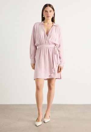 Wrap dress in light pink fabric with a deep V-neck, long sleeves, and a tie waist. Features a ruffled hem and vertical stripe texture.