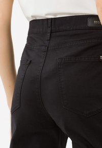 Pantaloni neri a vita alta realizzati in morbido tessuto di cotone. Presentano due tasche posteriori con un sottile bordo cucito.