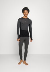 Långärmad svart och mörkgrå atletisk topp med åtsittande design och fuktavvisande tyg, parat med grå åtsittande leggings.