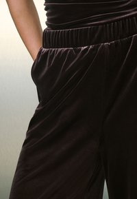 Mono de terciopelo negro con un corte holgado, que cuenta con una cintura elástica y bolsillos laterales. Textura suave con un brillo sutil.