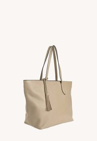 Sac fourre-tout en cuir beige avec deux longues poignées, présentant un détail de frange et un design minimaliste. Texture lisse et forme structurée.