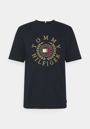 Granatowy bawełniany t-shirt z krótkimi rękawami, z dużym złoto-czerwonym logo "Tommy Hilfiger" otoczonym wzorem laurowym.
