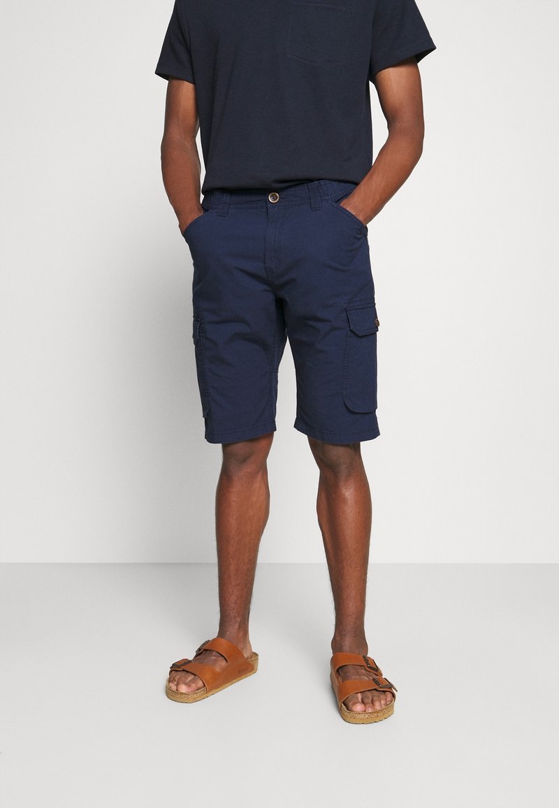 Bermuda cargo blu navy con tasche laterali, realizzate in misto cotone. Abbinati a una maglietta nera a maniche corte e sandali marroni.