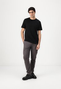 Camiseta negra de manga corta y pantalones cargo grises con bolsillos, combinados con zapatos negros con cordones. Diseño simple, ajuste moderno y colores neutros.