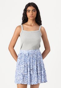 Grijze geribbelde tanktop met vierkante halslijn, gecombineerd met een lichtblauwe rok met bloemenpatroon in lagen. De rok heeft een elastische tailleband.