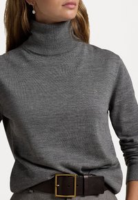 Grauer Rollkragenpullover aus strukturiertem Stoff, mit einem kleinen Logo auf der Brust. Kombiniert mit einem braunen Gürtel und einer goldenen Schnalle.