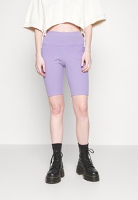 Lila cykelshorts i ribbad tyg, kombinerade med en kort vit topp. Modellen bär svarta snörstövlar med klumpiga sulor.