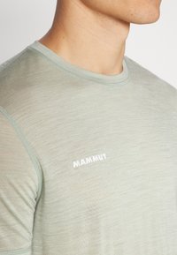 Lichtgroene T-shirt met korte mouwen, gemaakt van een gladde stof, met een subtiele textuur en een wit "MAMMUT" logo op de borst.