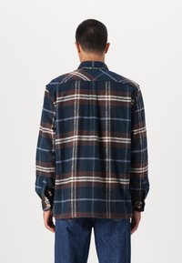 Camisa de flanela em padrão xadrez azul escuro, castanho e branco. Mangas longas, punhos com botão e um corte reto com textura suave.