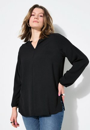 Zwarte langelijfde top met een V-hals, ontspannen pasvorm en gatherings bij de mouwen. Gelaagd stof en zijsplitten voor extra bewegingsvrijheid. Gekocht met blauwe jeans.