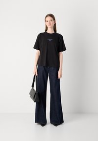 Black cotton t-shirt with a crew neckline and blue logo, paired with dark denim wide-leg jeans and a small black handbag.
