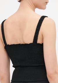 Zwart smock top met een crop lengte, dikke banden, een gestructureerd oppervlak en een ruffles aan de rand van de halslijn, gezien vanuit de achterkant.