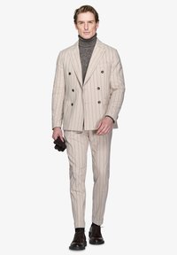 Completo beige chiaro a righe sottili con giacca doppiopetto e pantaloni abbinati. Indossato su un dolcevita scuro, completato con guanti marroni.