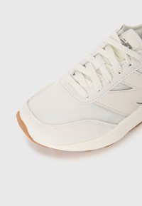 Weißer Sneaker von vorne mit einem Obermaterial aus Netzstoff, Wildlederbesatz, dicken weißen Schnürsenkeln und braunem Gummisohlenrand auf weißem Hintergrund.