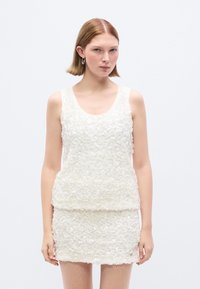 Λευκό αμάνικο τοπ με υφή και λουλουδένιο μοτίβο, συνδυασμένο με αντιστοιχία μίνι φούστα. Ομαλό ύφασμα με στρωμένα λεπτομέρειες.