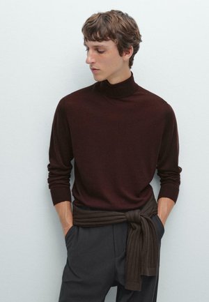 Maglione a collo alto marrone in maglia morbida, con maniche lunghe, abbinato a pantaloni grigi con cintura annodata di un marrone scuro, texture liscia, design aderente.