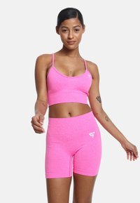 Ljusrosa träningsset bestående av en kortärmad tanktop och högmidjade shorts i sträckbart, texturerat tyg. Har en vit logotyp som accent.