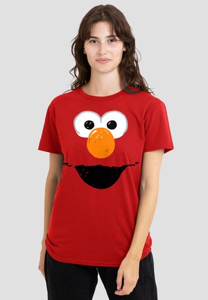 Red cotton t-shirt featuring a large, cartoonish graphic of a face with big eyes and an orange nose, set against a black smile design.
