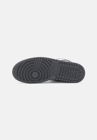 Semelle en caoutchouc noire d'une basket Nike affichant des motifs de crampons circulaires et en grille avec le logo Nike au centre.