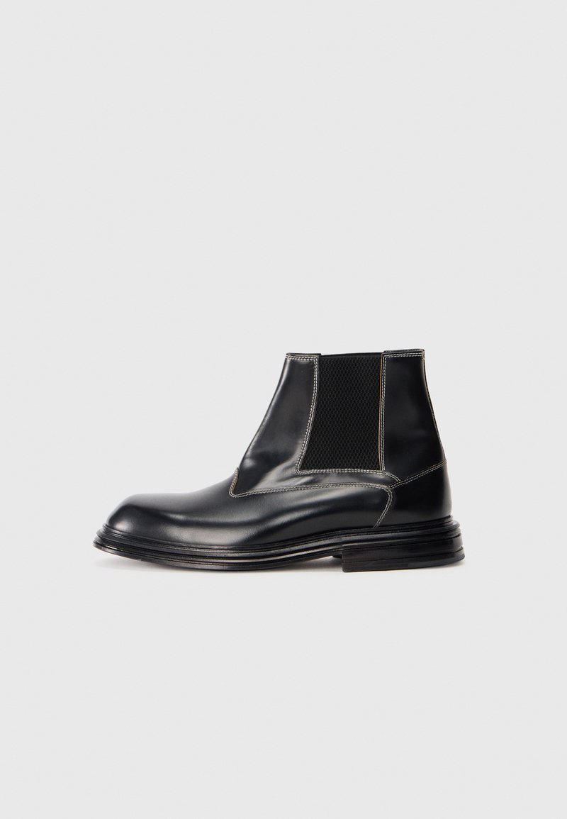 Bottines en cuir noir avec panneaux élastiques sur les côtés, bout arrondi et détails de couture contrastants. Accents en tissu texturé sur les côtés.