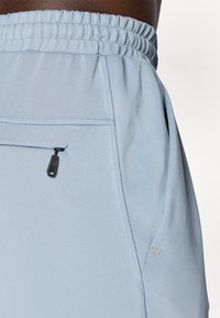Des pantalons de sport bleu clair présentent une taille élastique, une poche zippée et des coutures à plat pour plus de confort et de flexibilité.