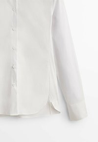 Chemise blanche à manches longues boutonnée, avec poignets et un ourlet arrondi avec une fente latérale.