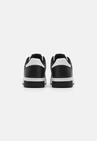 Schwarz-weiße Low-Top-Sneaker mit einem glatten Leder-Obermaterial, gepolstertem Kragen und strukturiertem Gummisohle, mit kontrastierenden weißen Akzenten.
