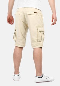 Beige cargo shorts with two side pockets, knee-length design, made from durable cotton material, paired with white sneakers.