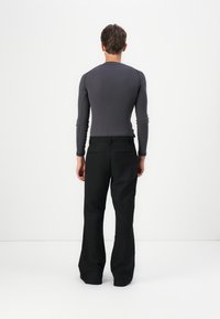 Šedý priliehavý top s dlhým rukávom a ribbed textúrou, kombinovaný s voľnými čiernymi nohavicami so bočnými vreckami a rovnými nohavicami.