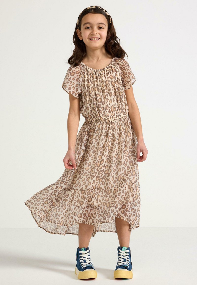 Beige jurk met luipaardprint, korte mouwen, elastische taille en gelaagde rok. Gepaard met blauwe sneakers en een bijpassend haarbandje.