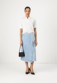 Hvit skjorte, lyseblå denim omslagskjørt, svarte høyhælte sko og en liten svart håndveske. Glatt stoff med et rent design.