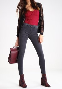 Röd spets bodysuit, svart spets cardigan, mörkgrå skinny jeans och mönstrade ankelboots. Bourgogne-handväska med ett spänne.