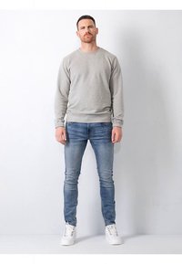 Ljusgrå sweatshirt med ribbade muddar och fåll, kombinerad med ljusblå jeans och vita sneakers. Avslappnad passform, minimalistisk design.