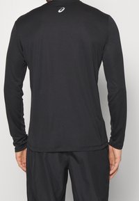 Mustan pitkähihainen urheilupaita, joka on valmistettu sileästä ja kevyestä kankaasta. Vaatteessa on pyöreä pääntie ja hillitty logoyksityiskohta yläselässä.