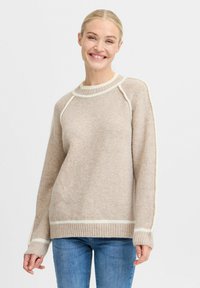 Beige trui van zacht materiaal, met een geribbelde onderkant en manchetten, en contrasterende witte details langs de halslijn en mouwen.