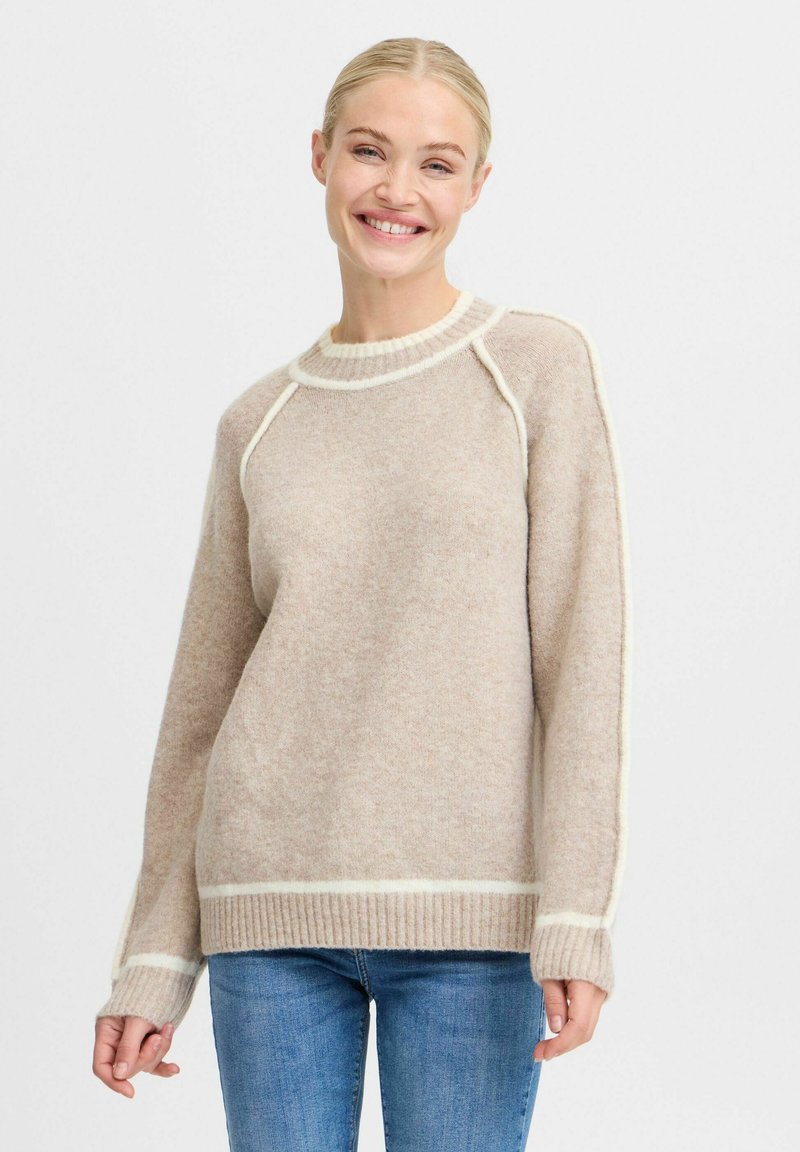 Beżowy sweter z miękkiego materiału, z prążkowanym dołem i mankietami oraz kontrastującymi białymi detalami wzdłuż dekoltu i rękawów.