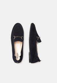 Mocassini in suede blu navy con un'accento di catena nera, tacco piatto e una morbida fodera interna. Caratterizzati da punta arrotondata e aperture elastiche.