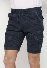Mörkblå cargo shorts i ett strukturerat, mönstrat tyg, med en elastisk midja och snörning. Inkluderar sid- och bakfickor.