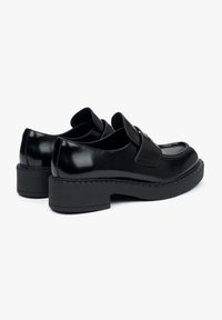 Czarne lakierowane buty z niskim obcasem, zaokrąglonym noskiem i dekoracyjnym przeszyciem. Posiadają pasek w okolicy języka.