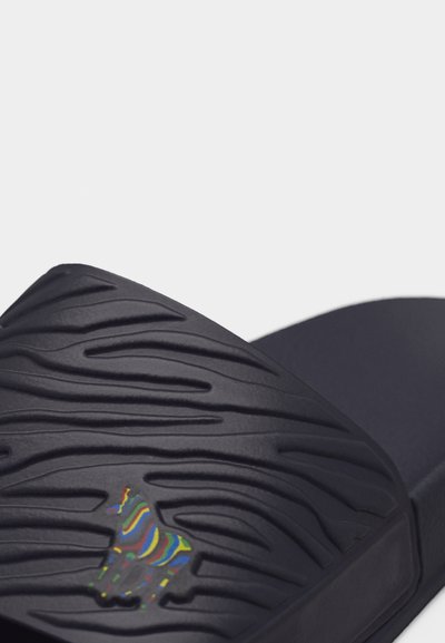 Κοντινή λήψη μαύρου σαγιοναριού με ανάγλυφες αυλακώσεις και μικρό πολύχρωμο λογότυπο ζέβρας στον ιμάντα.