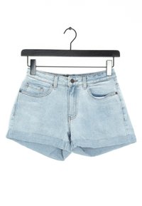 Pantalones cortos de mezclilla azul claro con dobladillo enrollado, que cuentan con dos bolsillos frontales y pasadores para cinturón. El material es suave y tiene una textura desgastada.