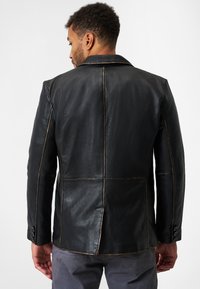Schwarze Lederjacke mit Reverskragen, sichtbaren Nähten und einem Schlitz auf der Rückseite. Glatte Textur mit tailliertem Schnitt und Knopfverschluss an den Ärmeln.