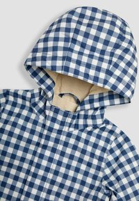 Giacca da pioggia a quadretti blu navy e bianca con cappuccio aderente e tessuto testurizzato e resistente all'acqua; include una fodera interna crema.