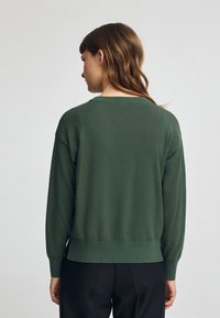 Pull vert à manches longues avec col rond, poignets et ourlet côtelés. Texture lisse, coupe légèrement ample et design minimaliste.