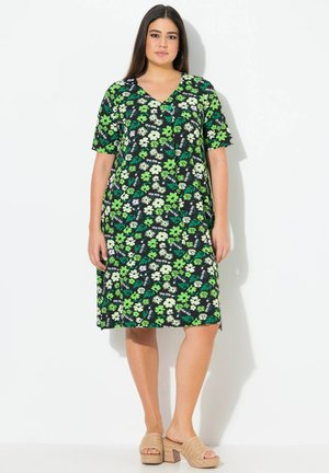 Blumenmusterkleid mit kurzen Ärmeln und V-Ausschnitt, mit grünen und weißen Blumen auf schwarzem Hintergrund. Kombiniert mit beigen Plateau-Mules.
