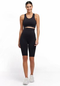 Completo activewear nero composto da un reggiseno sportivo aderente e pantaloni bike a vita alta, entrambi realizzati in un tessuto texture e con un branding discreto.