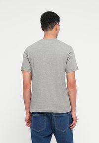 Γκρι β�αμβακερό μπλουζάκι με κοντά μανίκια, στρογγυλή λαιμόκοψη και ίσια γραμμή. Το ύφασμα έχει λεία υφή και μινιμαλιστικό σχέδιο.