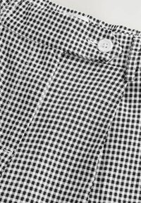 Tissu à carreaux noir et blanc avec de petits carrés ; présente une fermeture à bouton et une taille plate, mettant en valeur des lignes nettes et une texture soignée.