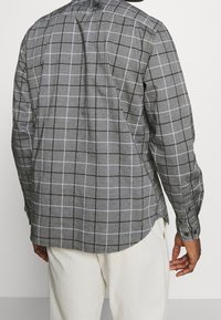 Camicia grigia a quadri con un motivo a griglia visibile, maniche lunghe, colletto a punta e polsini con bottoni, realizzata in un tessuto morbido e testurizzato.