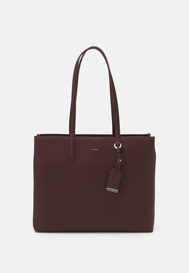 Burgundy läder tote-väska med två handtag, en slät yta, dragkedjestängning och en hängande tagg med en logotyp.